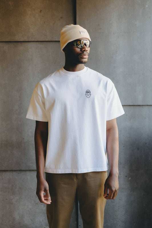 A man wearing a heavy overiszed white t-shirt, Oakley sunglasses and chalk beanie hat.